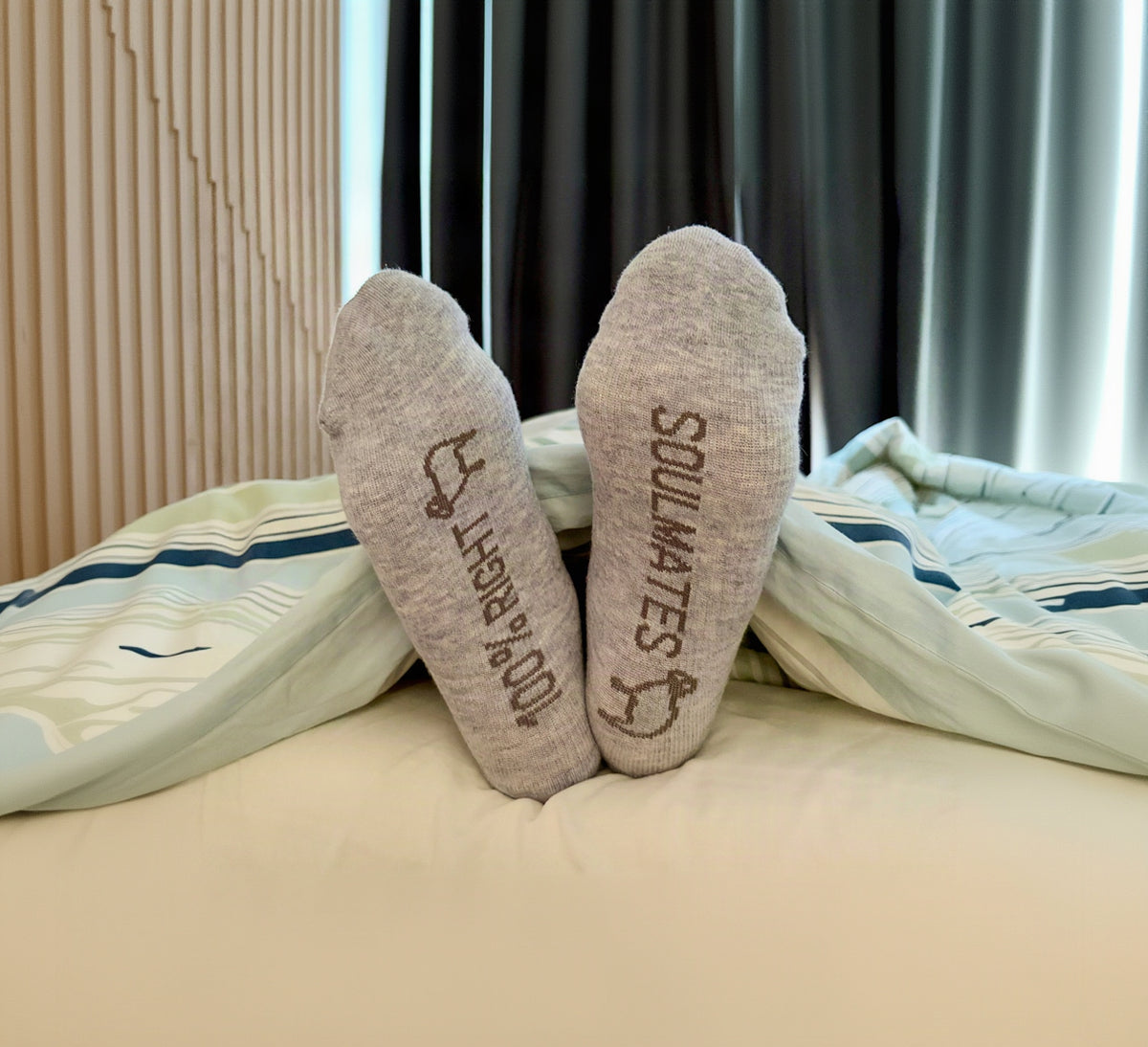 Grey compression socks with 100% RIGHT and SOULMATES sole prints, feet resting on a bed
