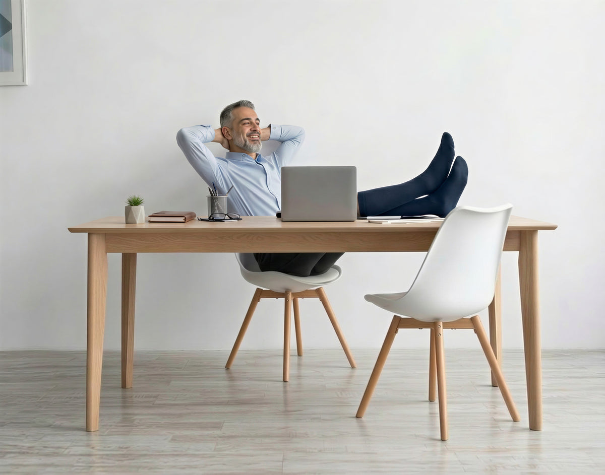 Man relaxing at his desk with his feet up, wearing navy knee-high compression socks
