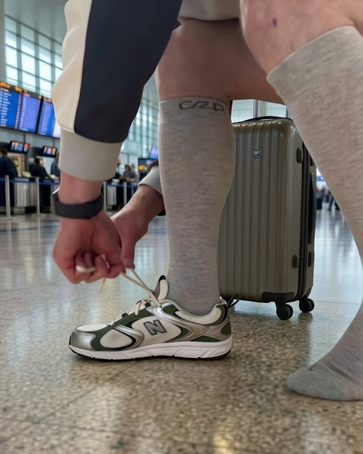Traveller tying trainers at the airport in grey knee-high compression socks